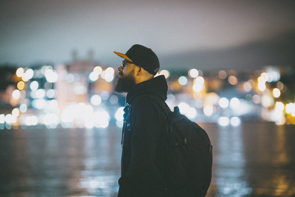 man in black hoodie and yellow cap standing near body of water during night time