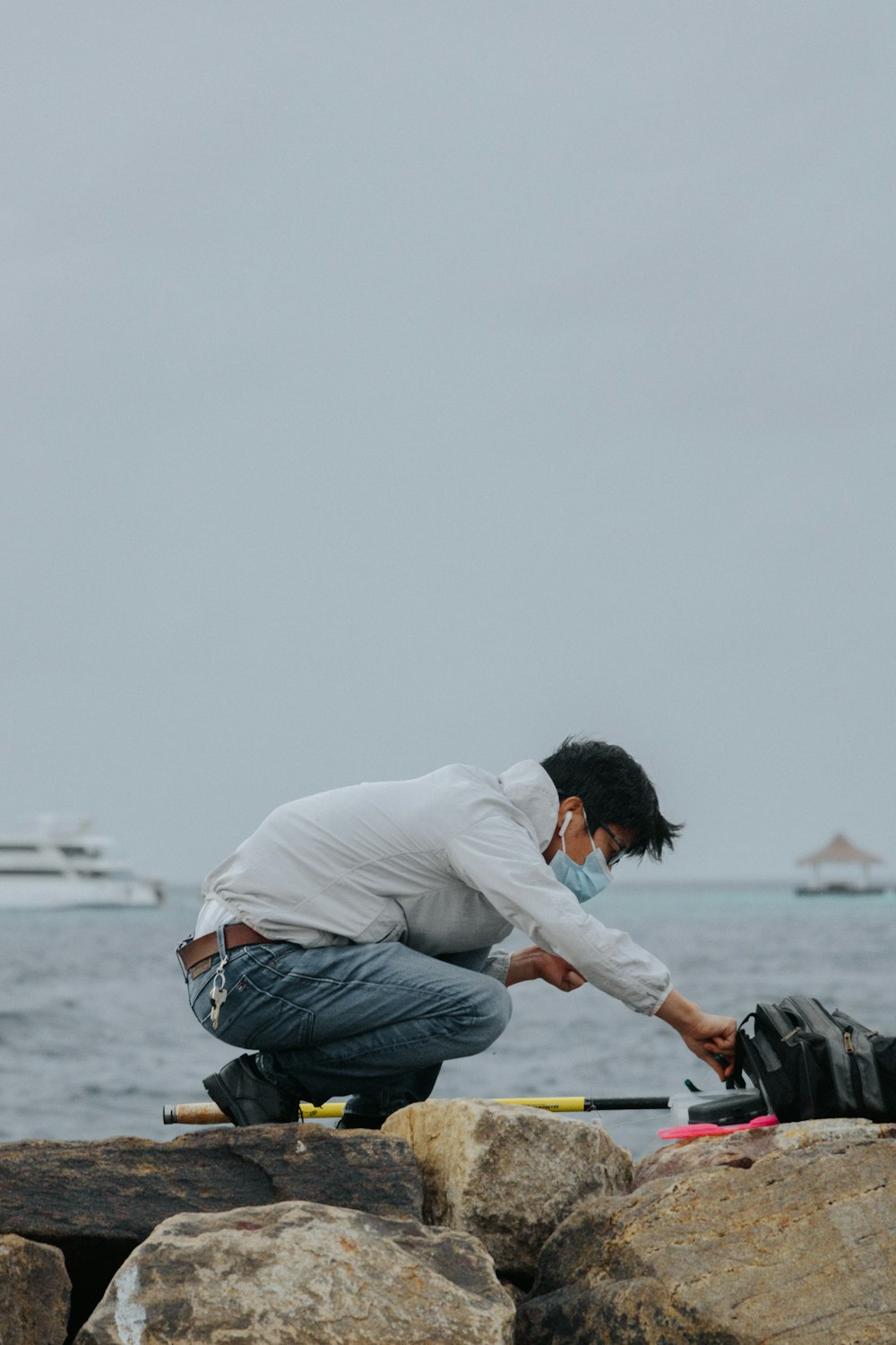 man in white dress shirt and blue denim jeans sitting on rock near sea during daytime