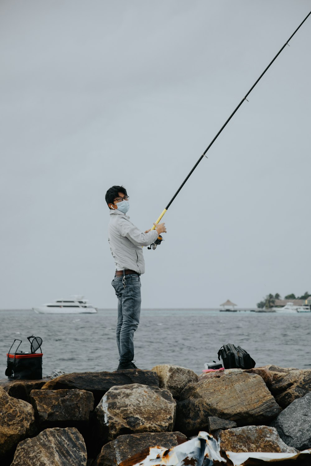 man in white dress shirt and blue denim jeans holding fishing rod standing on brown rock