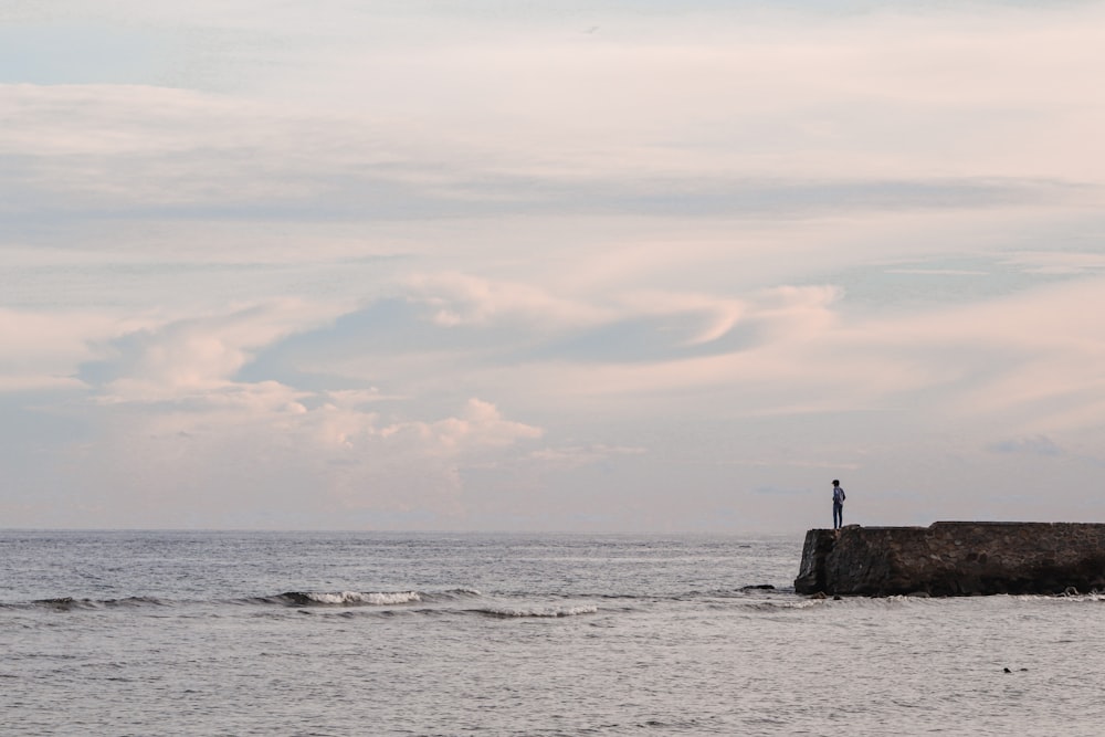 silhouette of person standing on rock formation in the middle of sea during daytime
