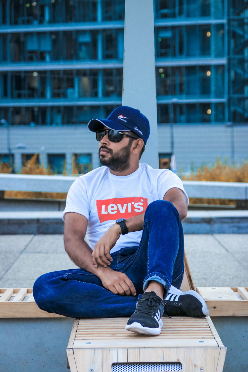 Hombre con camiseta blanca de cuello redondo y jeans de mezclilla azules sentado en un banco de madera marrón