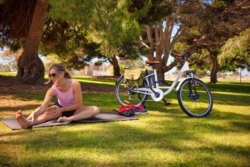 woman in pink tank top sitting on green grass field near bicycle during daytime