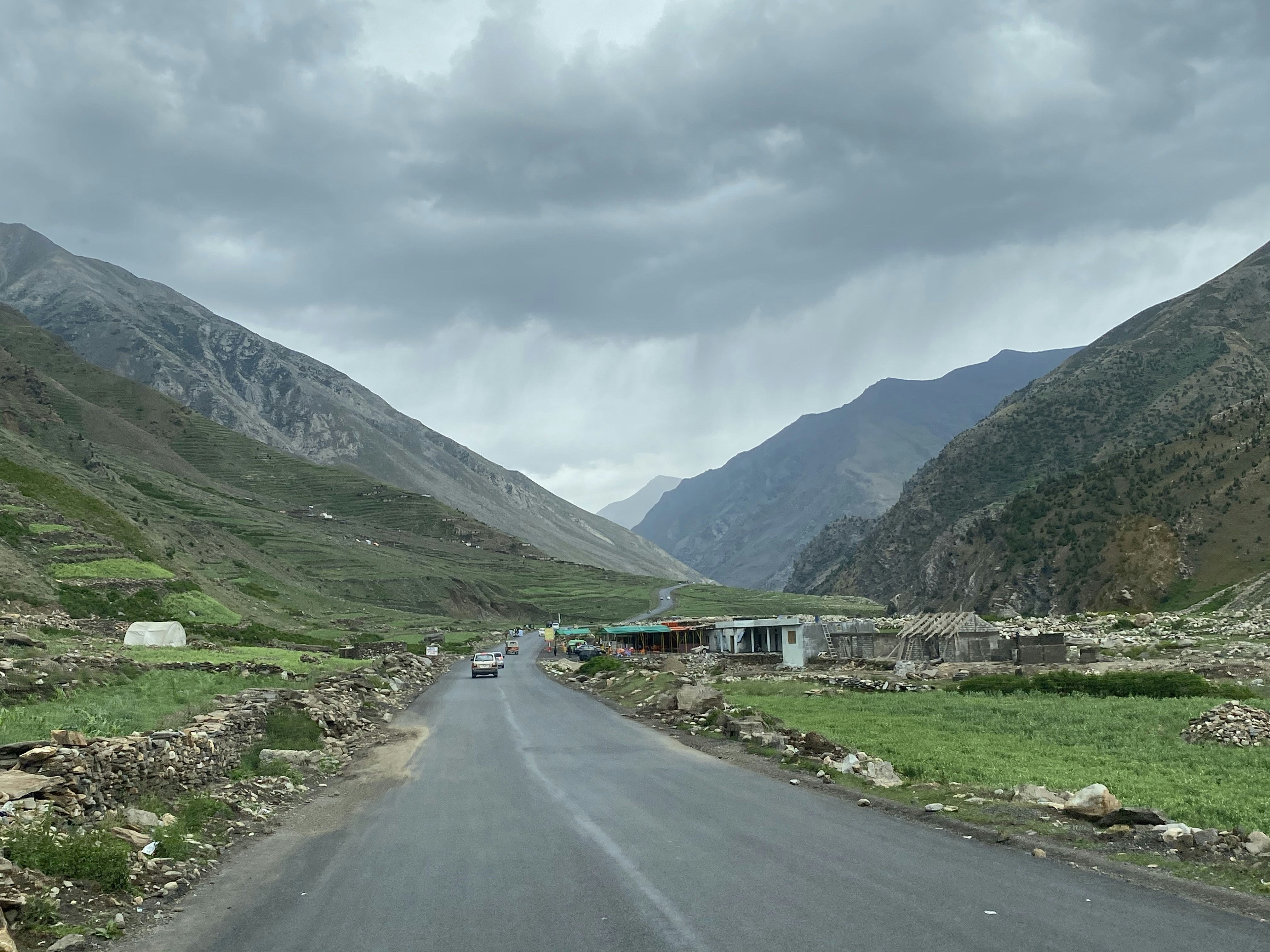 gray asphalt road between green grass field near mountain under white cloudy sky during daytime