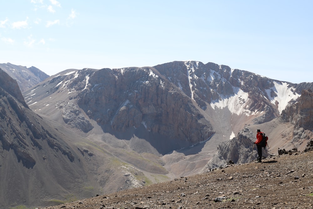 person in red jacket standing on brown field near gray rocky mountain during daytime