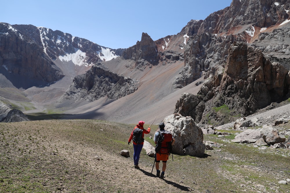 2 person walking on dirt road near mountain during daytime