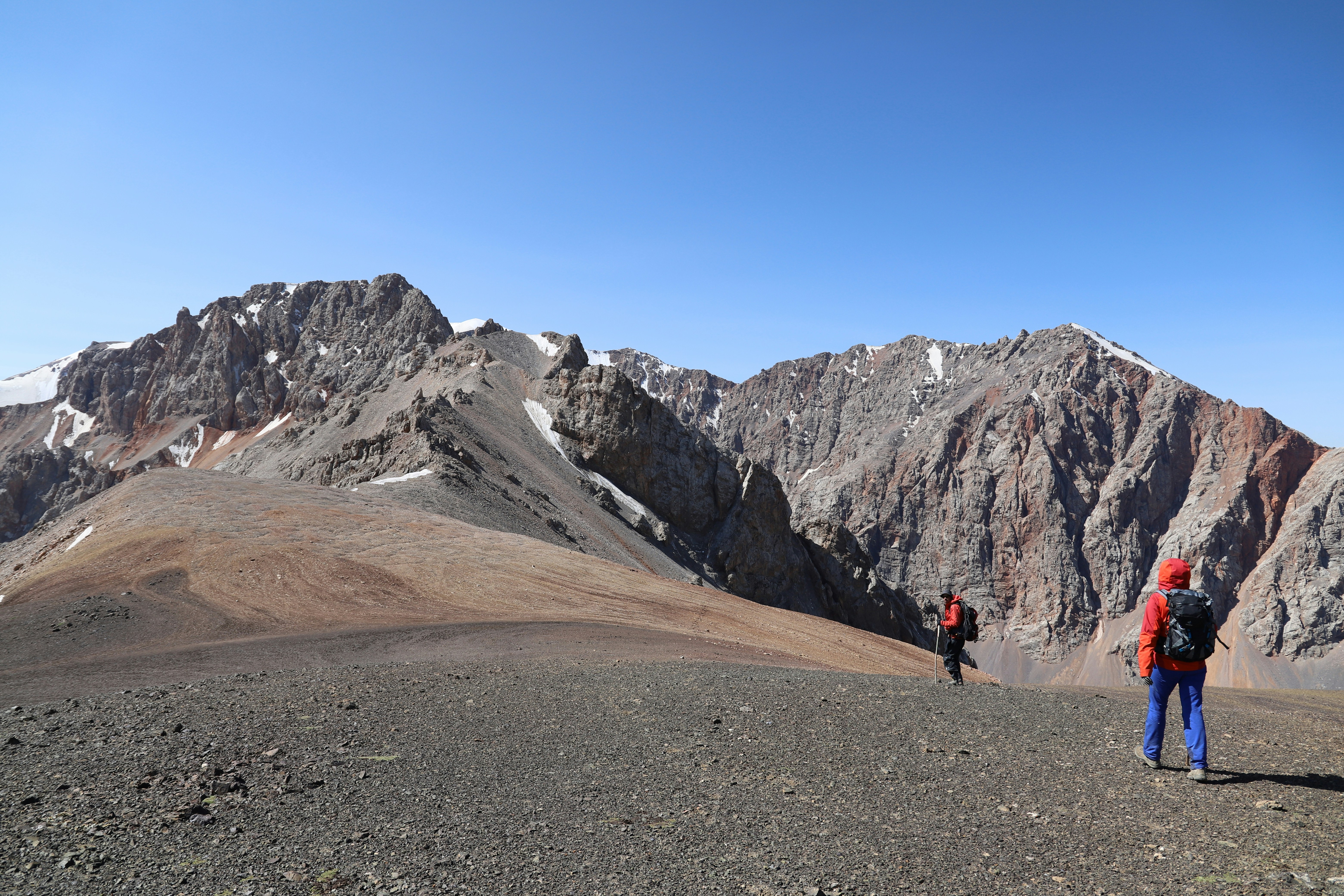 person walking on brown dirt road near gray rocky mountain under blue sky during daytime