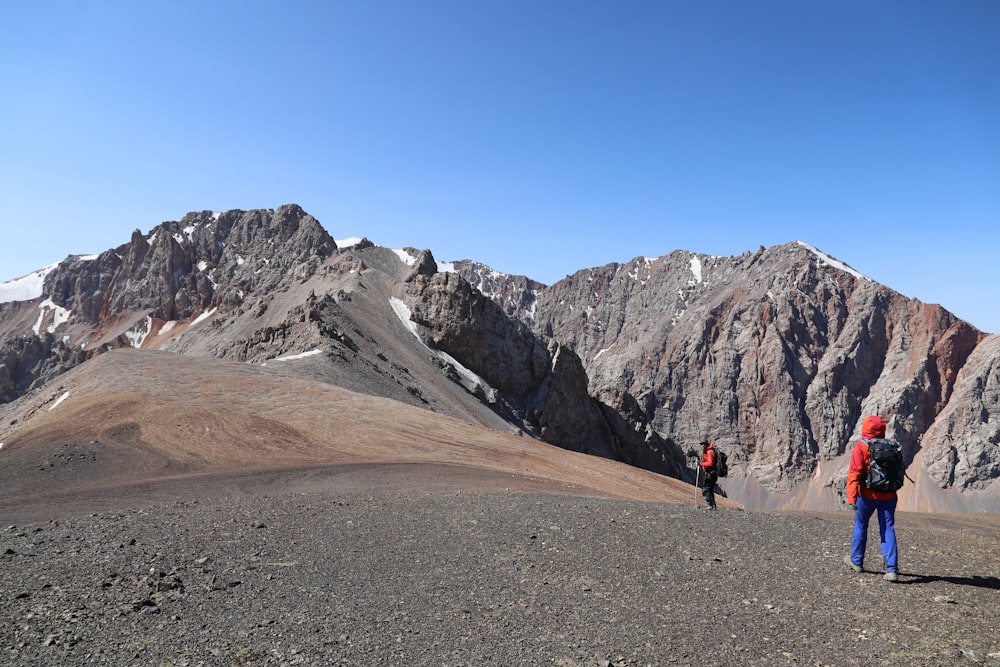 person walking on brown dirt road near gray rocky mountain under blue sky during daytime