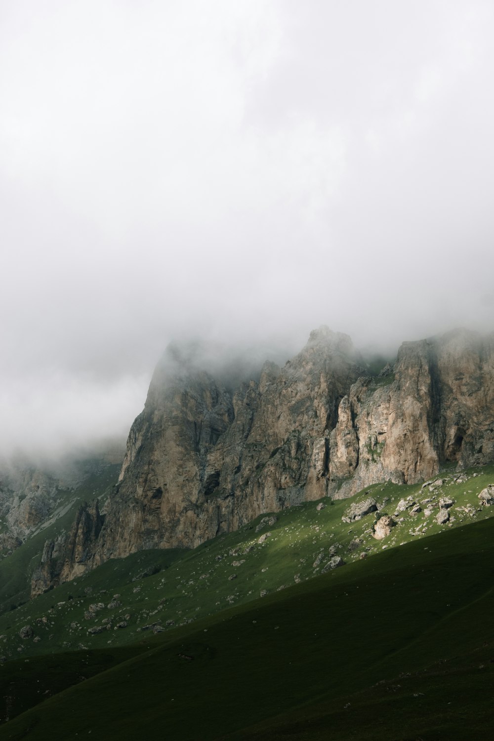 green grass field near brown rocky mountain during foggy day