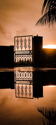 A sturdy wrought iron gate with intricate detailing guarding a driveway at sunset.