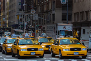 yellow taxi cab on road near white concrete building during daytime