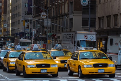 yellow taxi cab on road near white concrete building during daytime