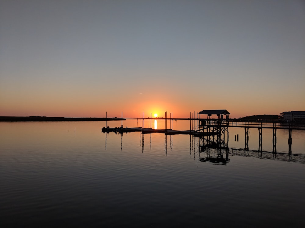 silhouette of dock on calm water during sunset