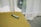 A vape pen with a black and light blue color scheme rests on a mustard yellow upholstered surface. Natural light streams through sheer white curtains in the background, creating a soft, inviting ambiance.