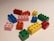 A collection of colorful LEGO blocks scattered on a light-colored surface, featuring various colors such as red, blue, green, yellow, pink, and orange. The blocks vary in size and are arranged randomly, creating a playful and vibrant scene.