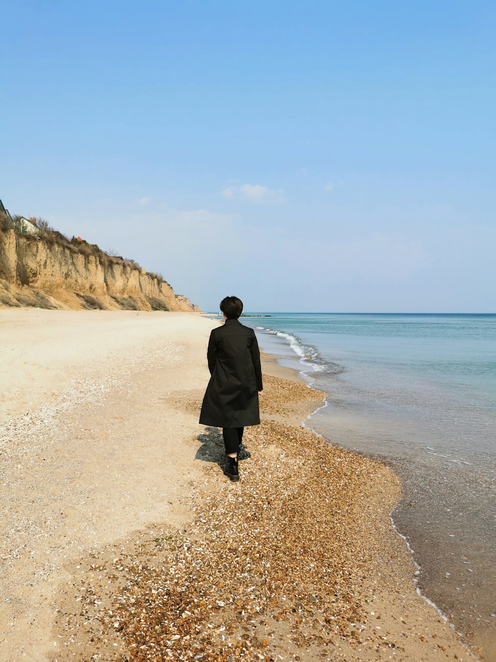 man in black coat standing on brown sand near body of water during daytime
