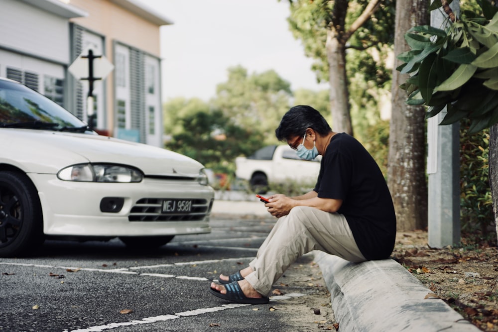 man in black t-shirt and gray pants sitting on gray concrete pavement during daytime