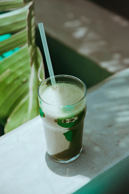 Close-up of a happy person enjoying a green smoothie in a sunlit kitchen