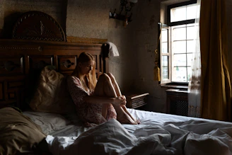 Softly lit photo of a woman in a handwoven cotton nightgown, sitting by a window with morning light.