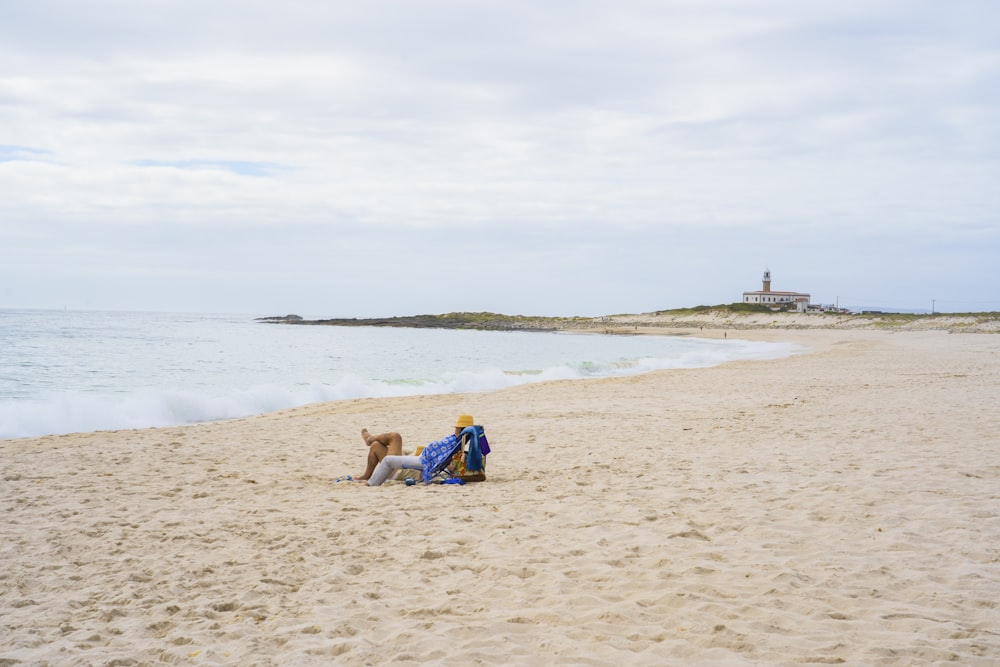 woman in blue and white dress sitting on brown sand near body of water during daytime