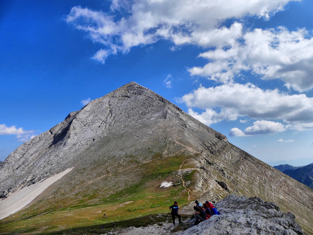 people sitting on ground near mountain under blue sky during daytime