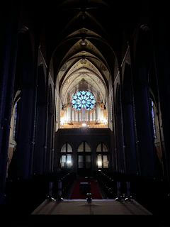 A dimly lit cathedral interior with stained glass windows casting colorful light on a choir singing in harmony.