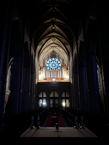 A dimly lit cathedral interior with stained glass windows casting colorful light on a choir singing in harmony.