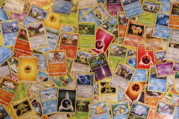 A collection of assorted Pokémon trading cards spread out, displaying various Pokémon characters, energies, and abilities. The cards vary in type, color, and design, showcasing different Pokémon species, stats, and features.