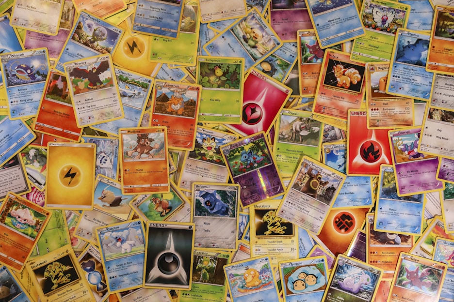 A collection of assorted Pokémon trading cards spread out, displaying various Pokémon characters, energies, and abilities. The cards vary in type, color, and design, showcasing different Pokémon species, stats, and features.