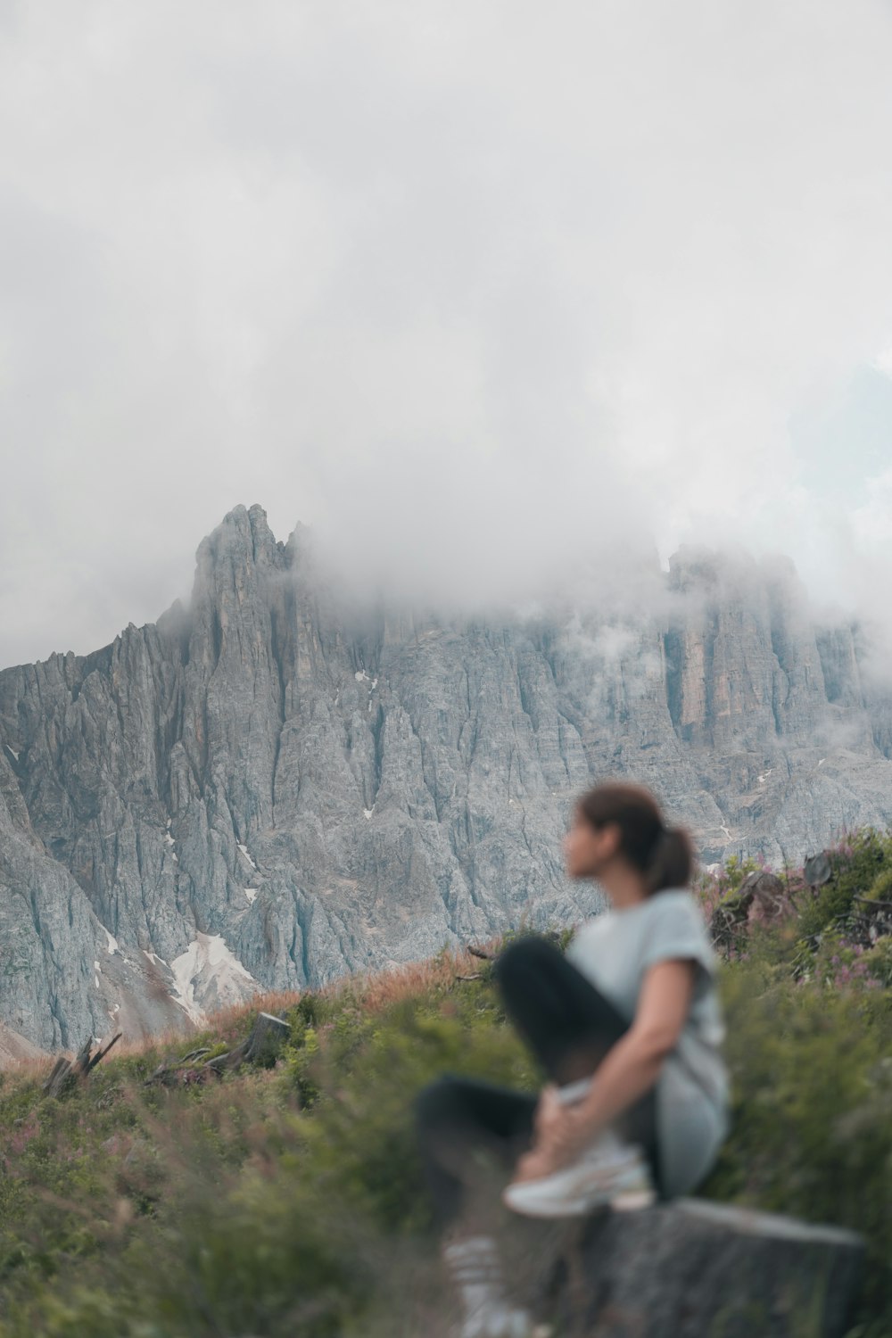 mulher na camisa branca de pé no campo verde da grama perto da montanha rochosa cinzenta durante o dia
