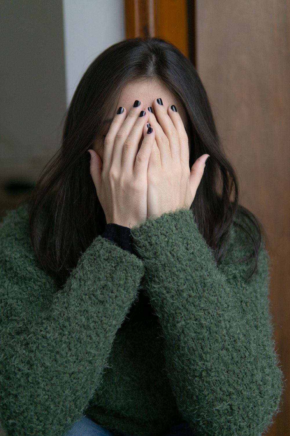 woman in green sweater covering her face with her hand