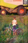 a young boy standing next to a bike in a field