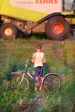 a young boy standing next to a bike in a field