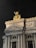 A grand architectural facade featuring intricately detailed sculptures and columns. A golden statue of a winged figure stands prominently atop a richly decorated pediment, with the word 'CHOREGRAPHIE' etched below. The structure is illuminated against a dark night sky, highlighting its classical design and ornate embellishments.