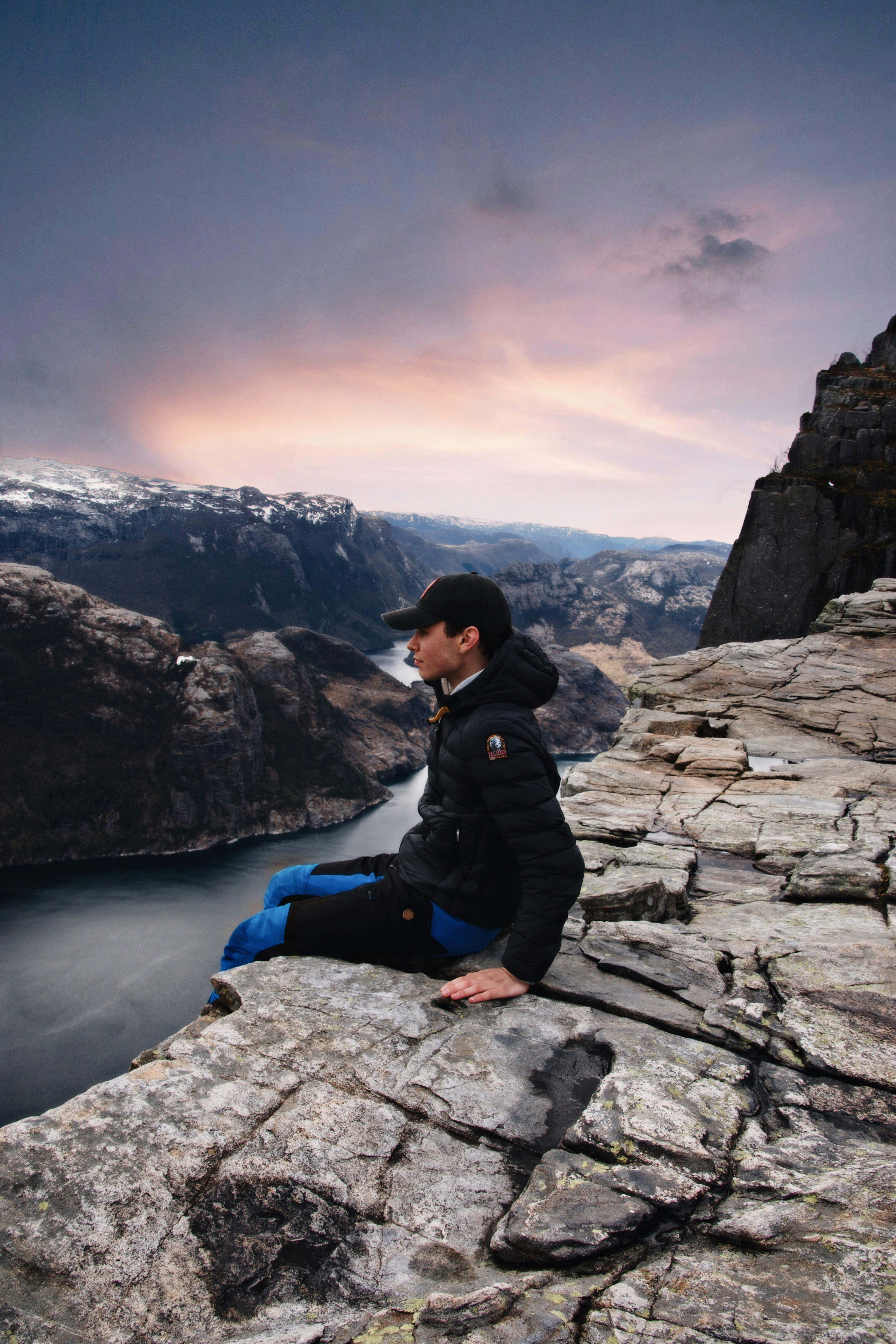 woman in black jacket and blue denim jeans sitting on rock formation near lake during daytime