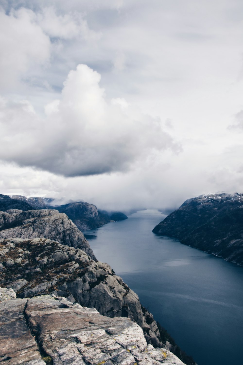 Montaña rocosa gris cerca del cuerpo de agua bajo nubes blancas durante el día