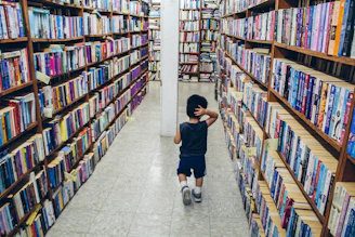 A boy walking through the library with shelves of books in the background