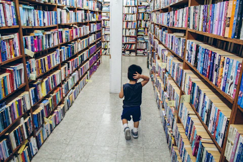 A boy walking through the library with shelves of books in the background