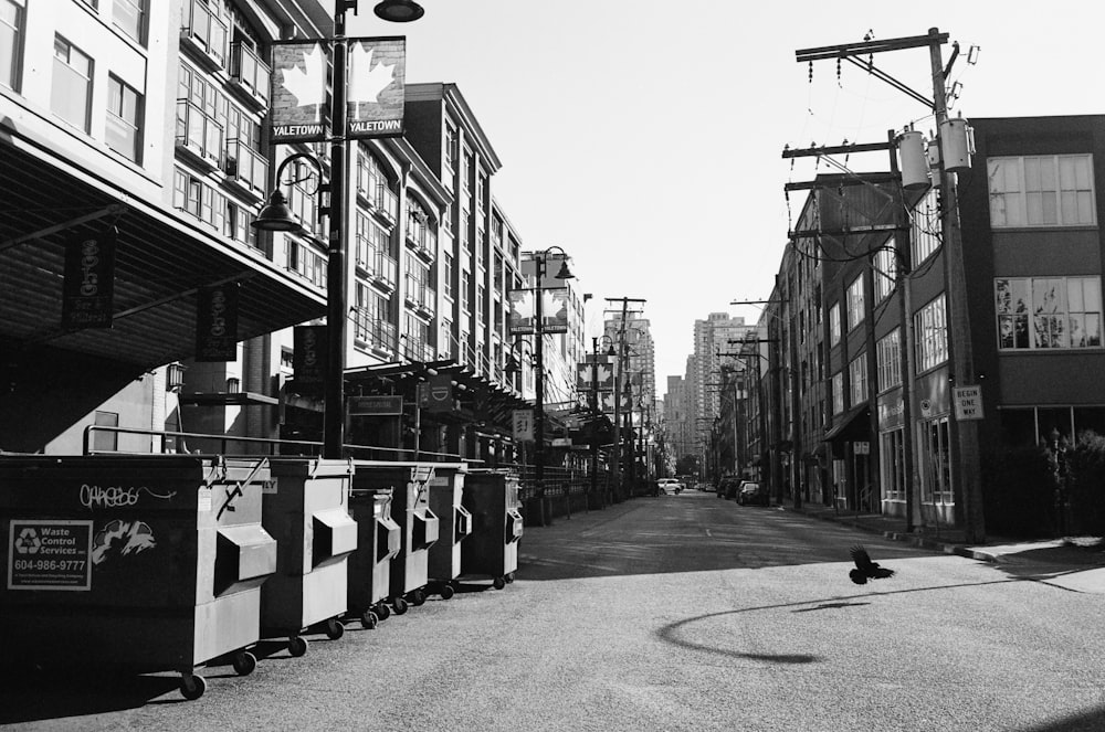 grayscale photo of street with cars parked beside buildings