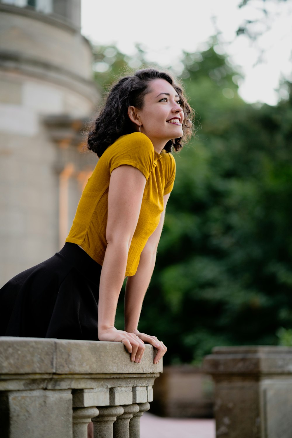 a woman in a yellow shirt leaning on a wall