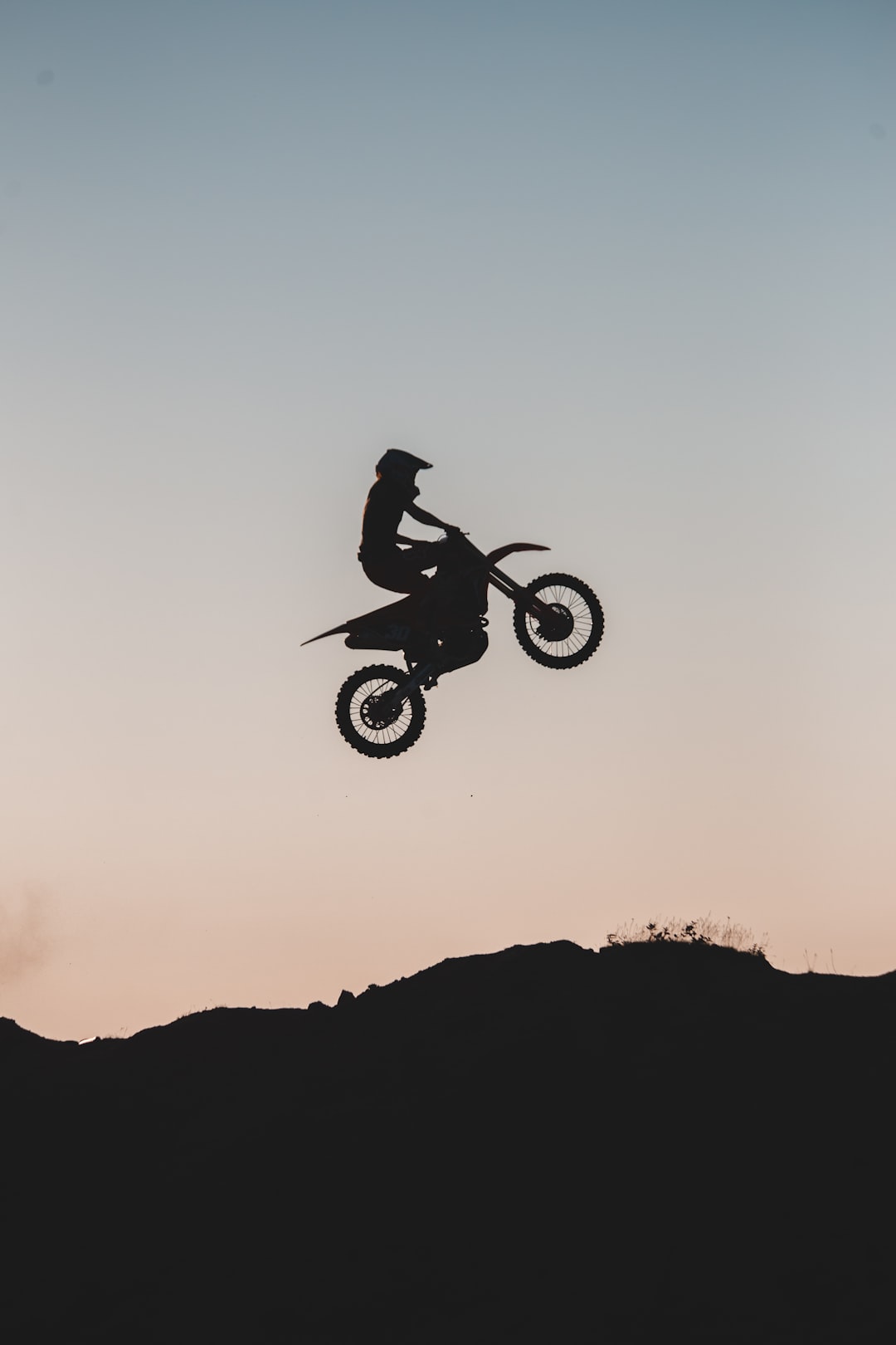 silhouette of man riding motocross dirt bike on mid air during sunset