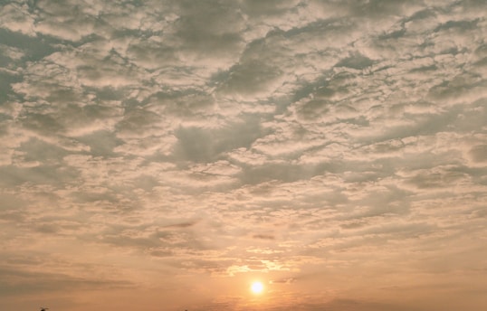 A soft sunrise breaking gently through scattered clouds, casting warm golden light over a peaceful landscape.