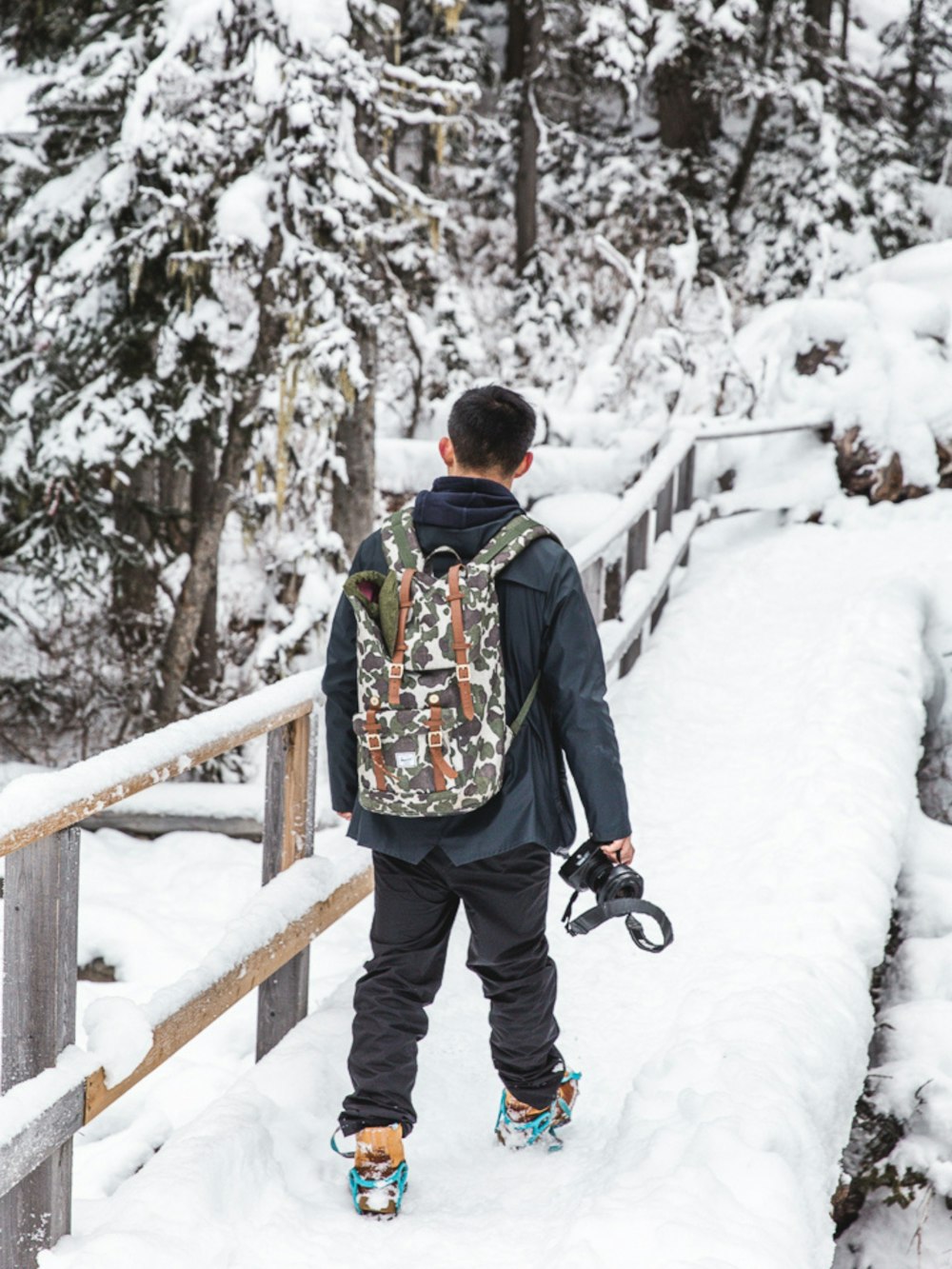 Mann in schwarzer Jacke und brauner Hose, der tagsüber auf schneebedecktem Boden steht