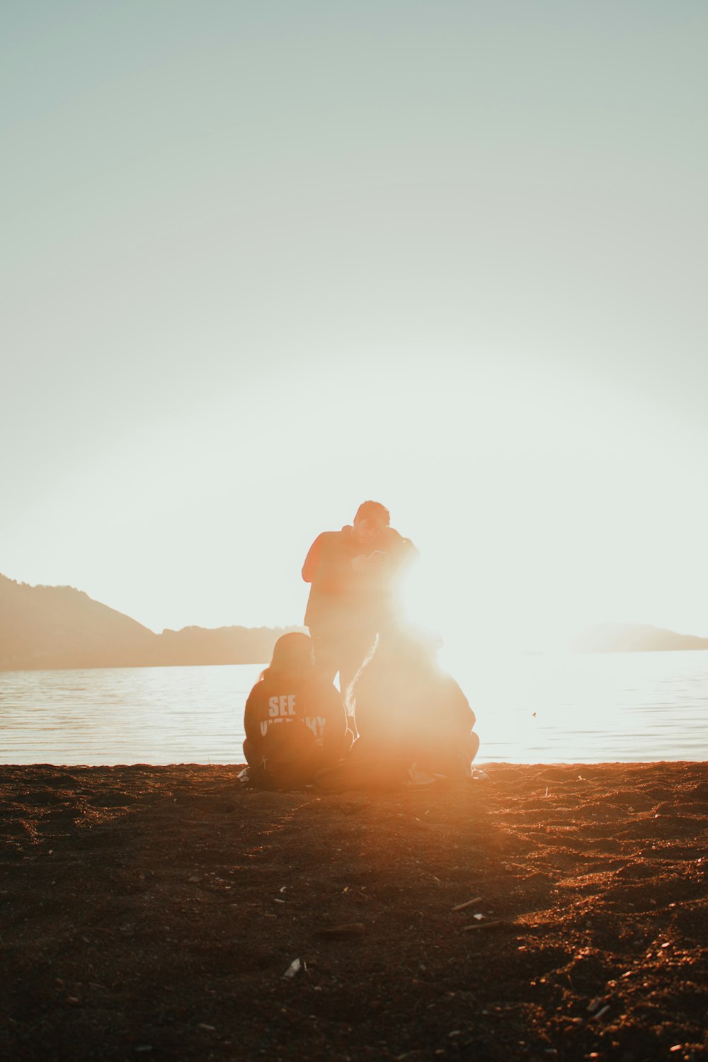 silhouette of man sitting on rock near body of water during sunset