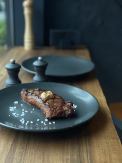 A beautifully plated steak with garnishes on a dark wooden table.