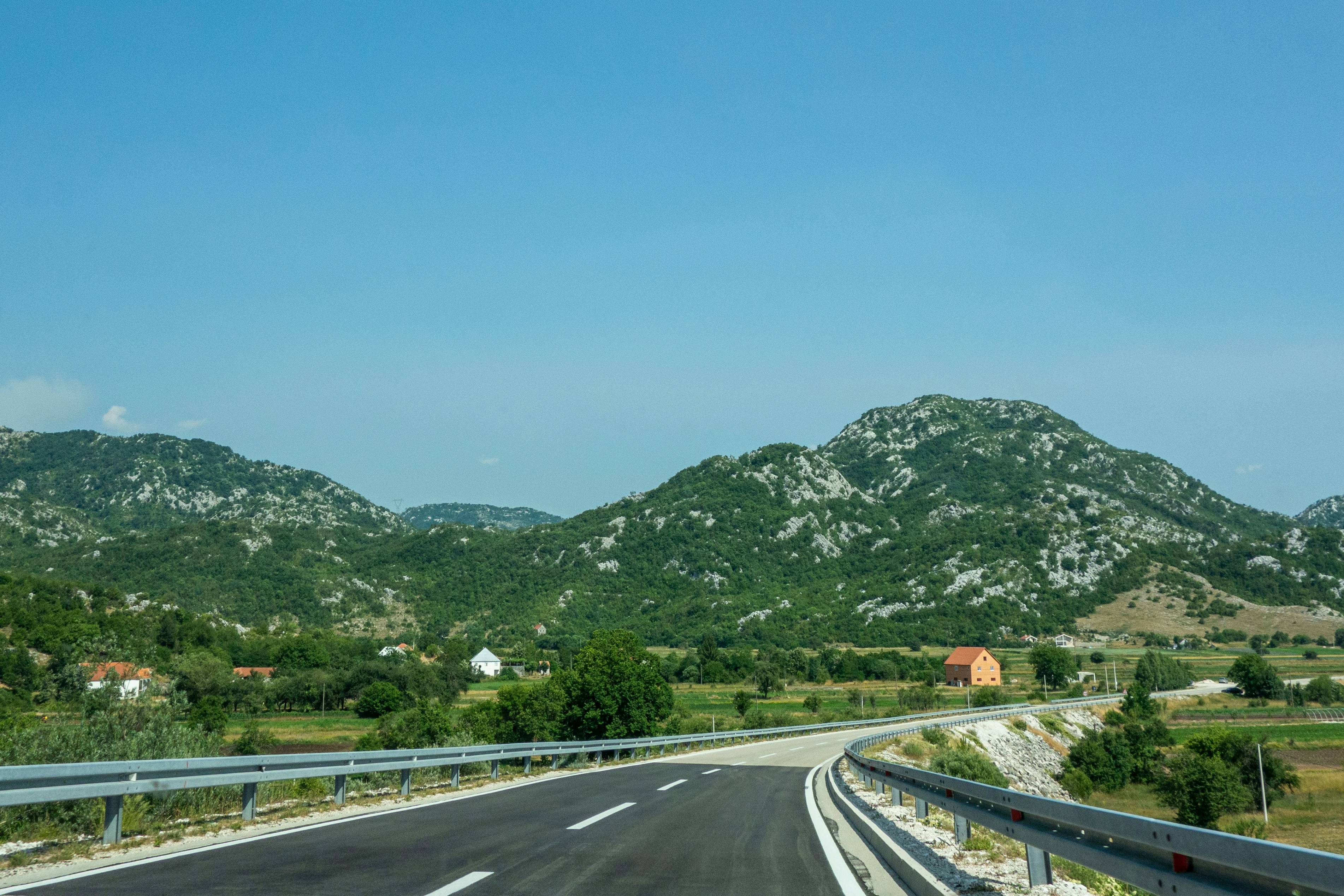 gray concrete road near green mountain under blue sky during daytime