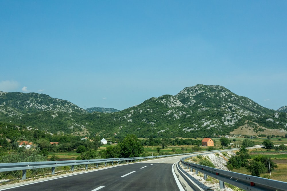 gray concrete road near green mountain under blue sky during daytime