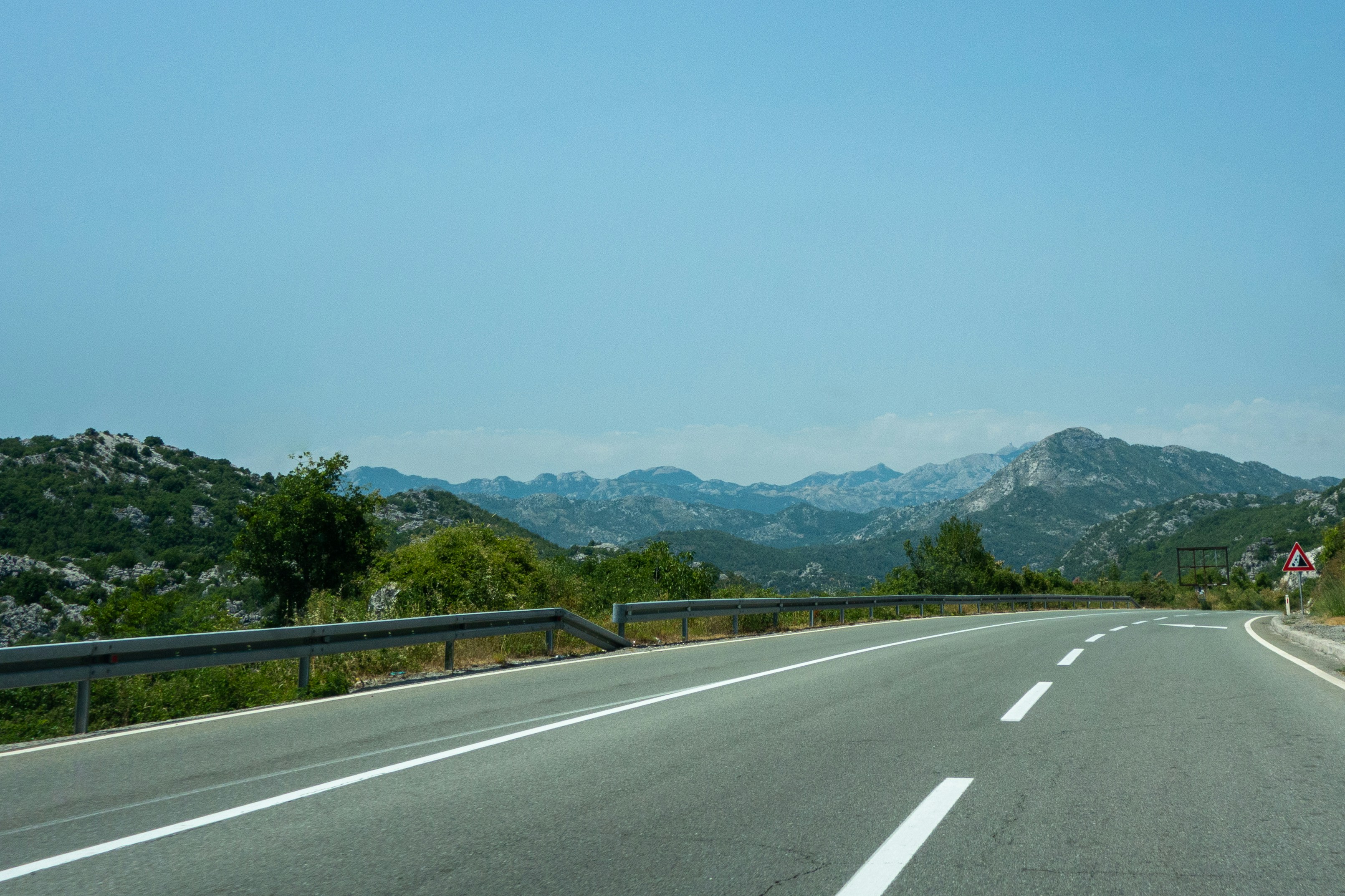 gray concrete road near green trees and mountain during daytime