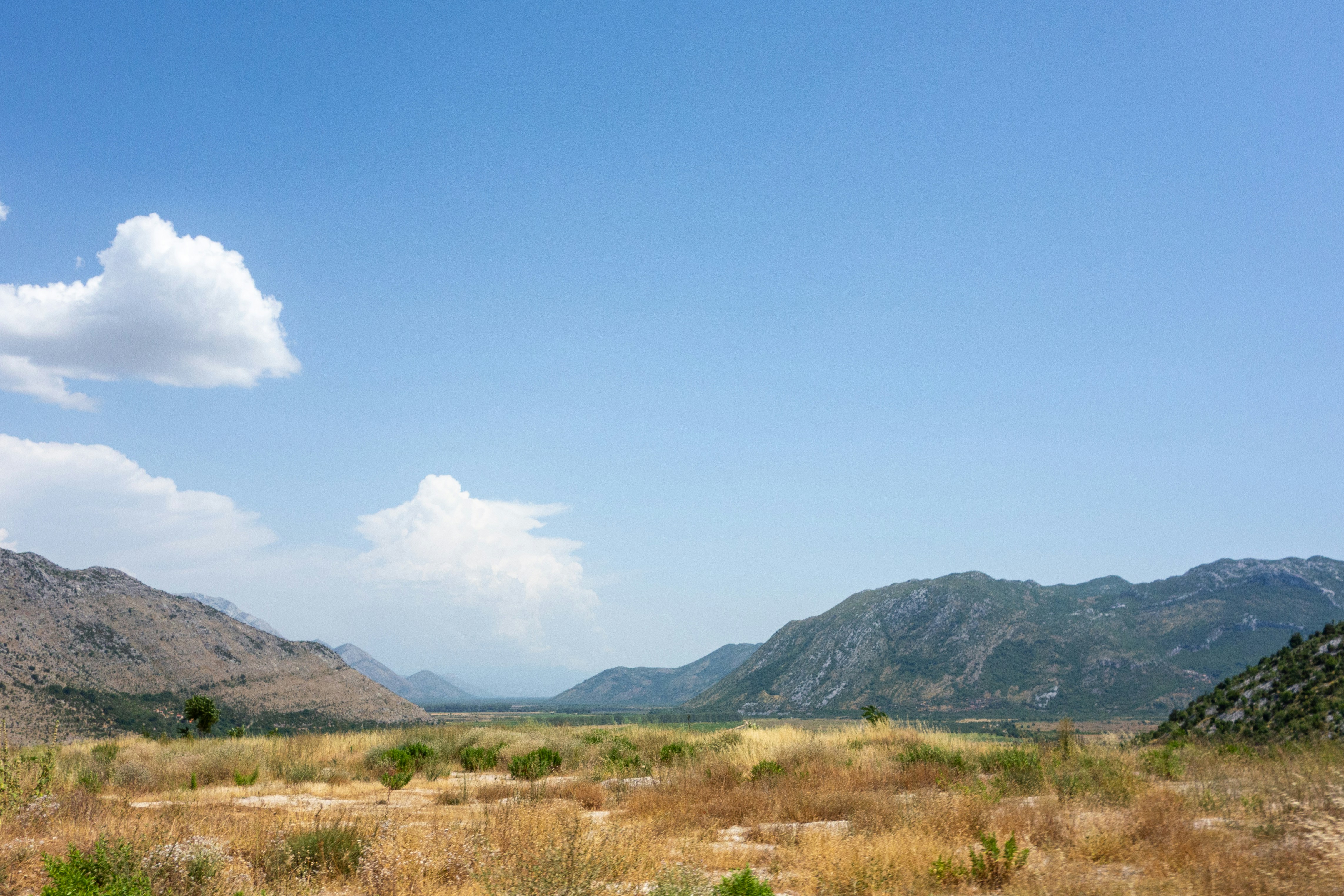 green grass field near mountain under blue sky during daytime, Driving through Bosnia and Herzegovina.