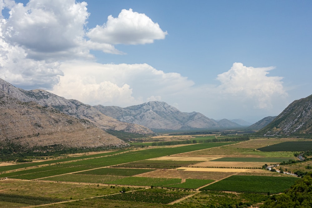 green grass field near mountains under white clouds and blue sky during daytime