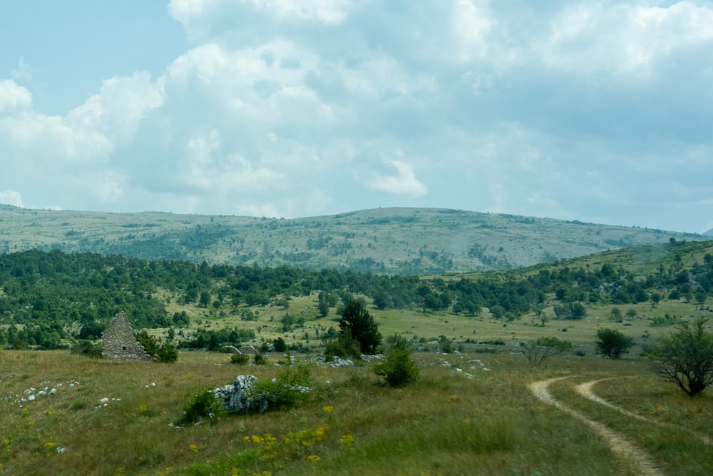 green grass field near green mountains under white clouds during daytime